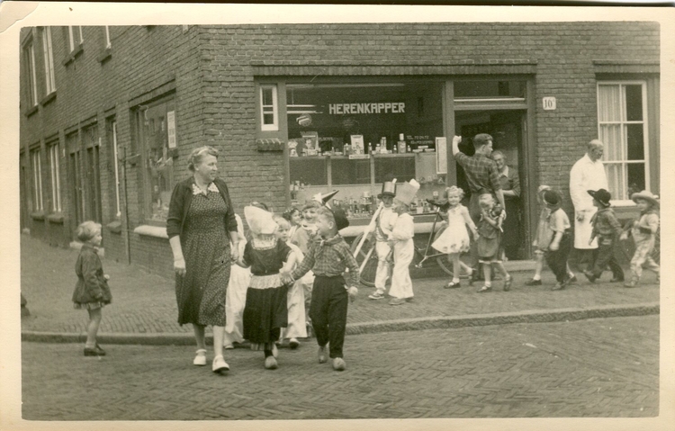 Buurtwinkel Diamanstraat 10a, 1956.  <p>Op deze foto is te zien dat er in het pand een kapperszaak zat in de jaren ´50 van de vorige eeuw. Op de voorgrond is een juffrouw te zien met een klas. Het is een verkleedfeest van de kleuterschool vanwege een jongen, genaamd Chris, die vijf jaar is geworden.</p>